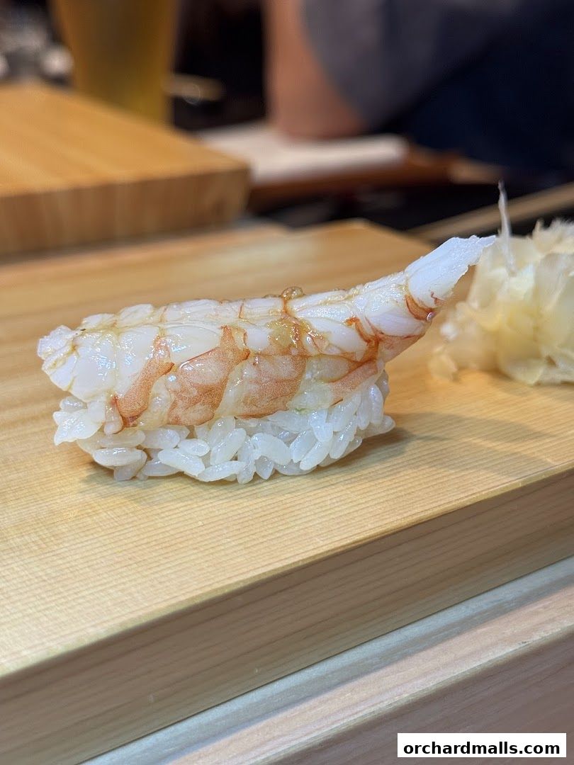 A close-up of a delicious shrimp sushi piece served on a wooden board.