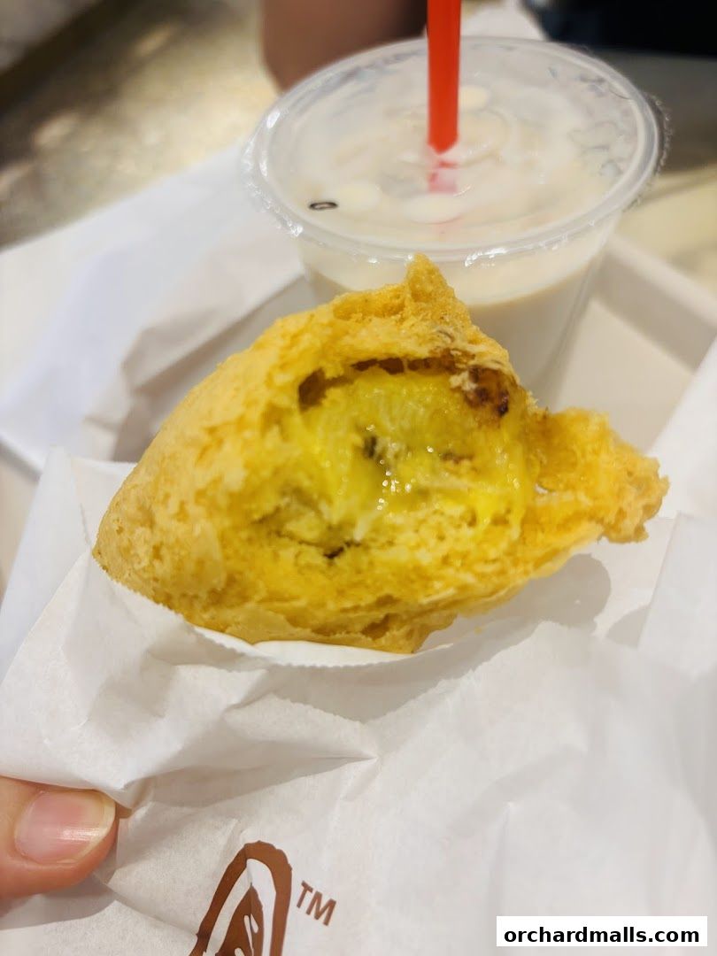 A close-up of a golden-fried fritter with a drink in the background.