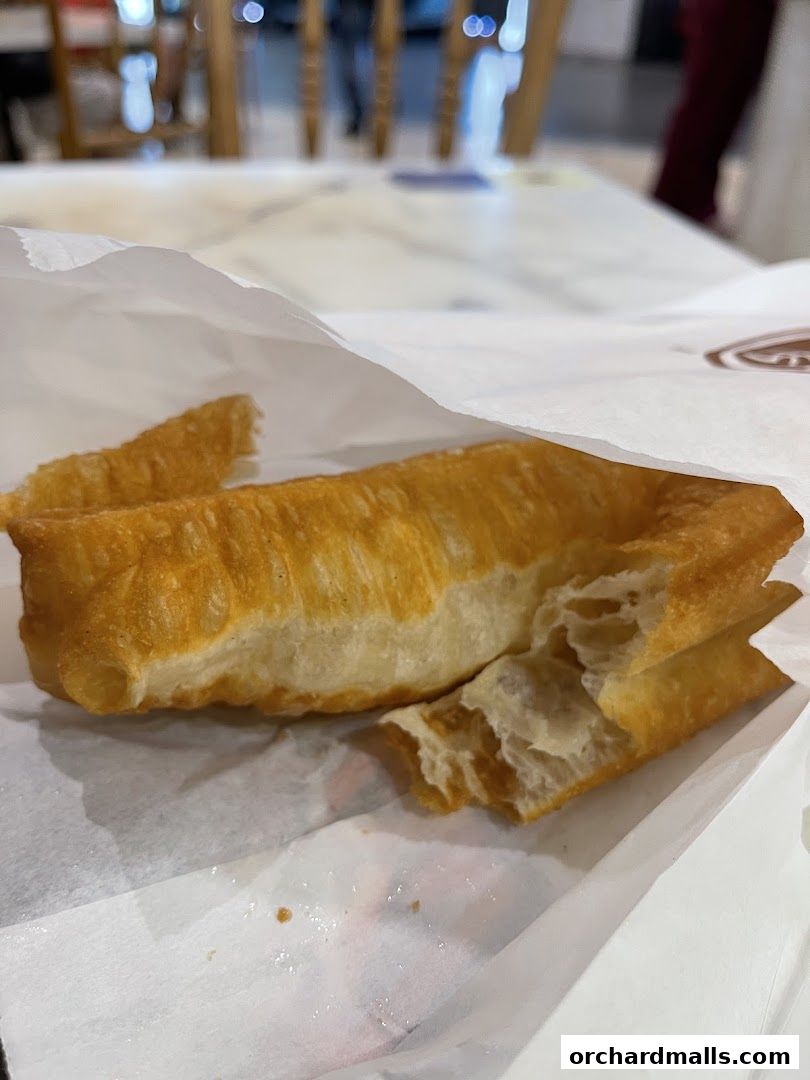 A close-up shot of golden-brown fried fritters in a white paper bag.