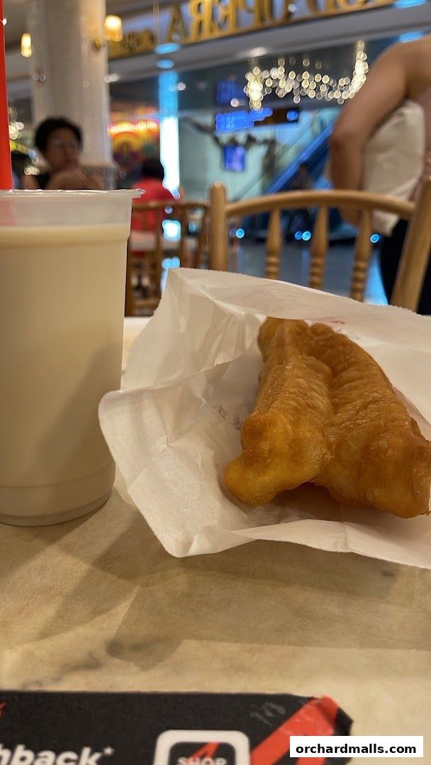 A cup of soy milk and fried dough sticks on a table at a food stall.