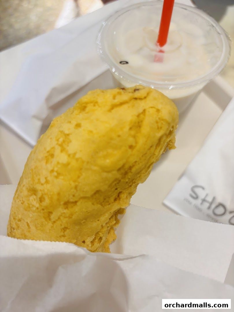 A golden-brown fried fritter and a drink with a red straw on a white tray.