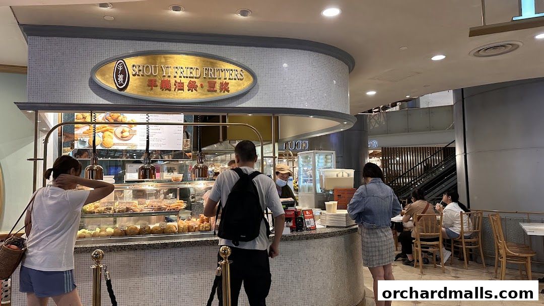 Customers queue at Shou Yi Fried Fritters, a food stall with a display of fried snacks.