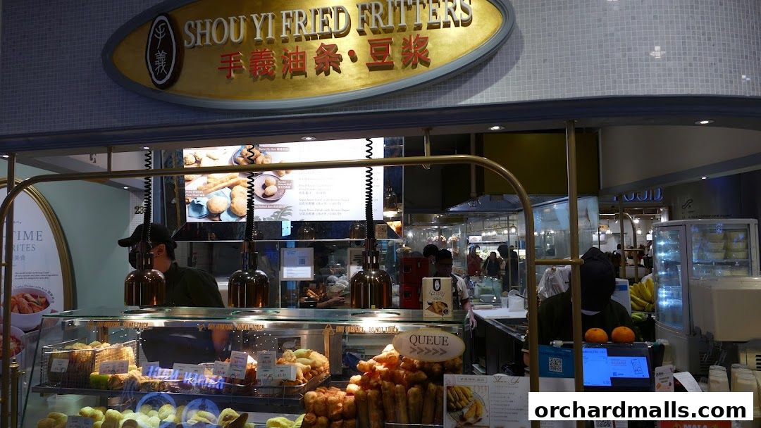 A display of fried fritters and other food items at a shop counter with a prominent sign.