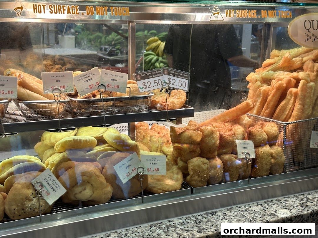 A display case filled with various fried fritters and pastries, with price labels visible.