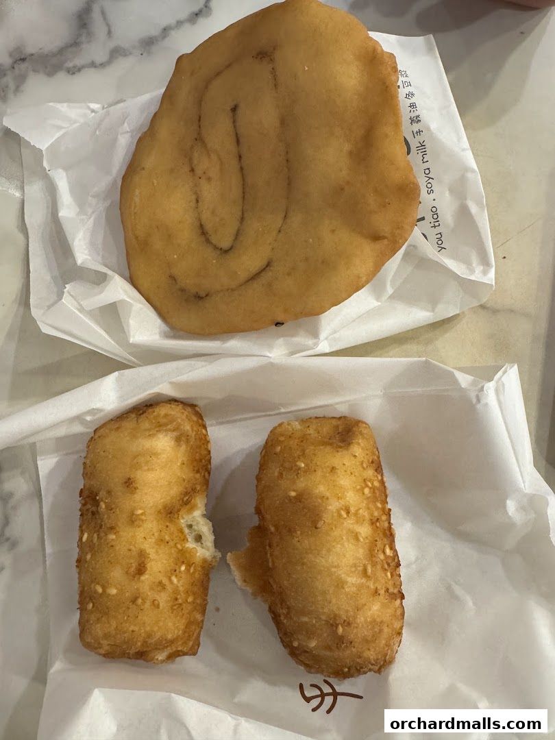 Two types of fried fritters, one large and flat with cinnamon swirls, and two smaller ones coated in sesame seeds.