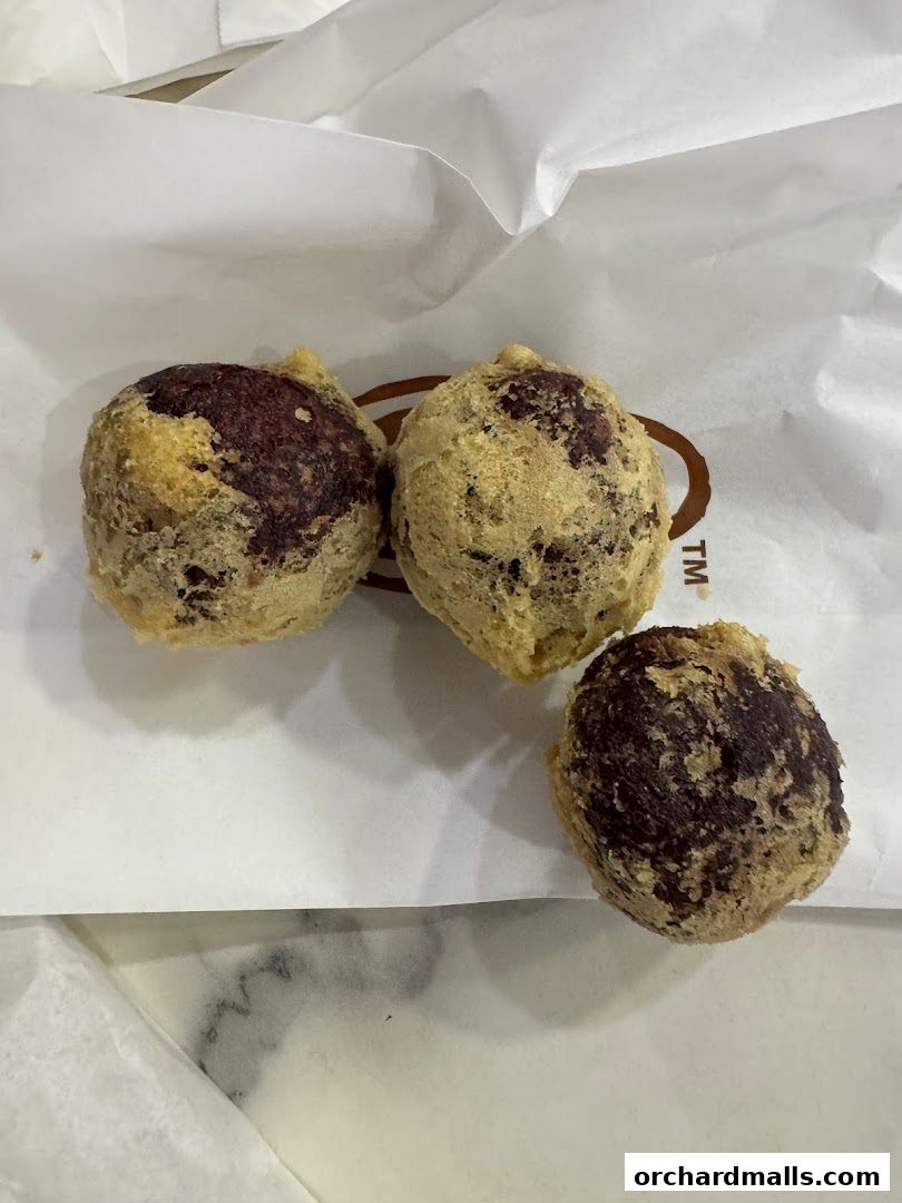 Three golden-brown fried fritters with a dark filling, served on white paper.
