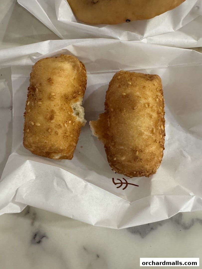 Two golden fried fritters with sesame seeds, served on white paper.
