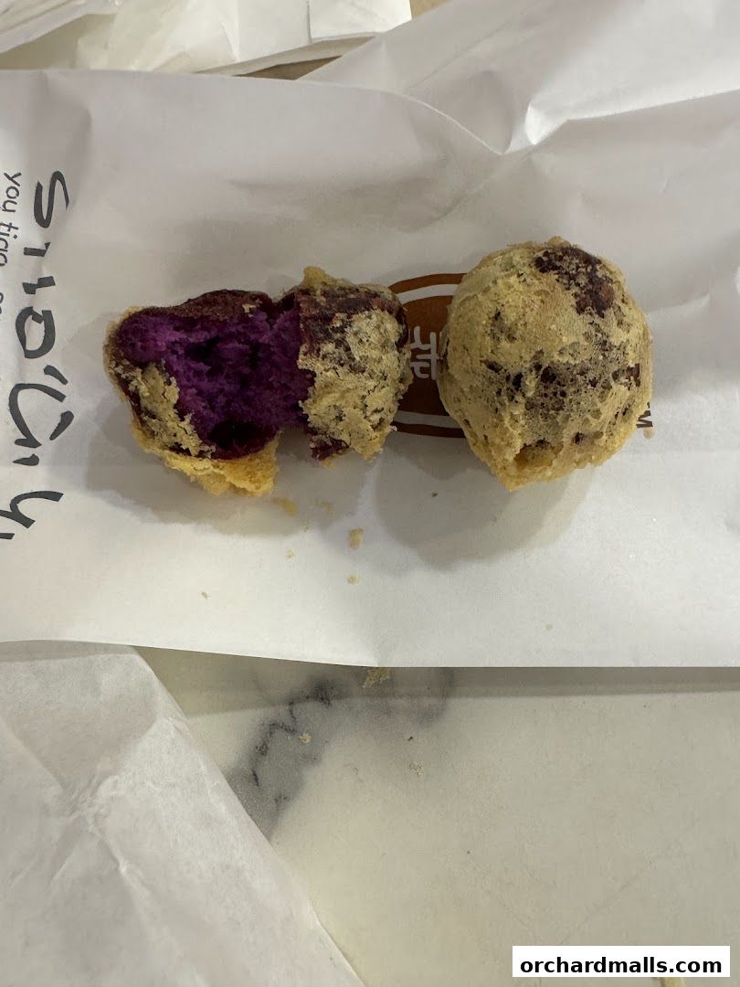 Two fried fritters, one split open revealing a vibrant purple interior, on white paper.