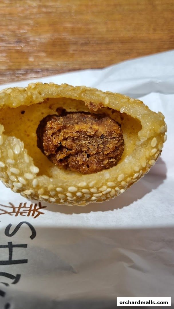 A close-up of a sesame seed fritter with a savory filling, presented on white paper.