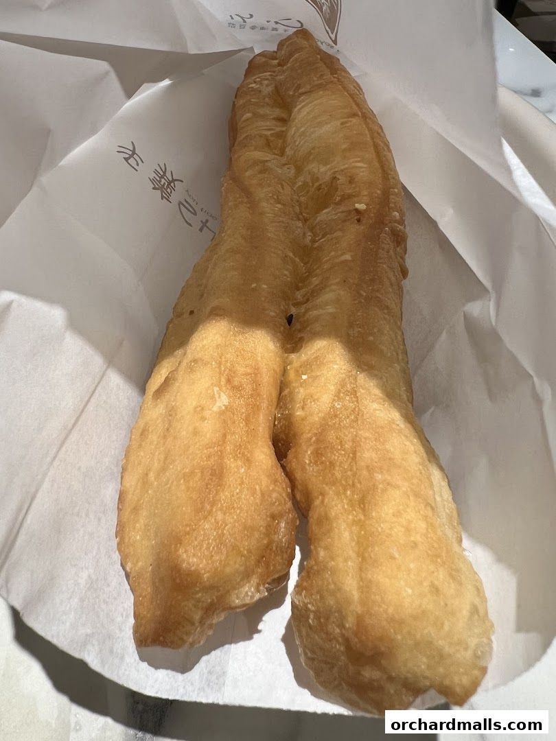 A close-up shot of a golden-brown fried dough fritter in a white paper bag.