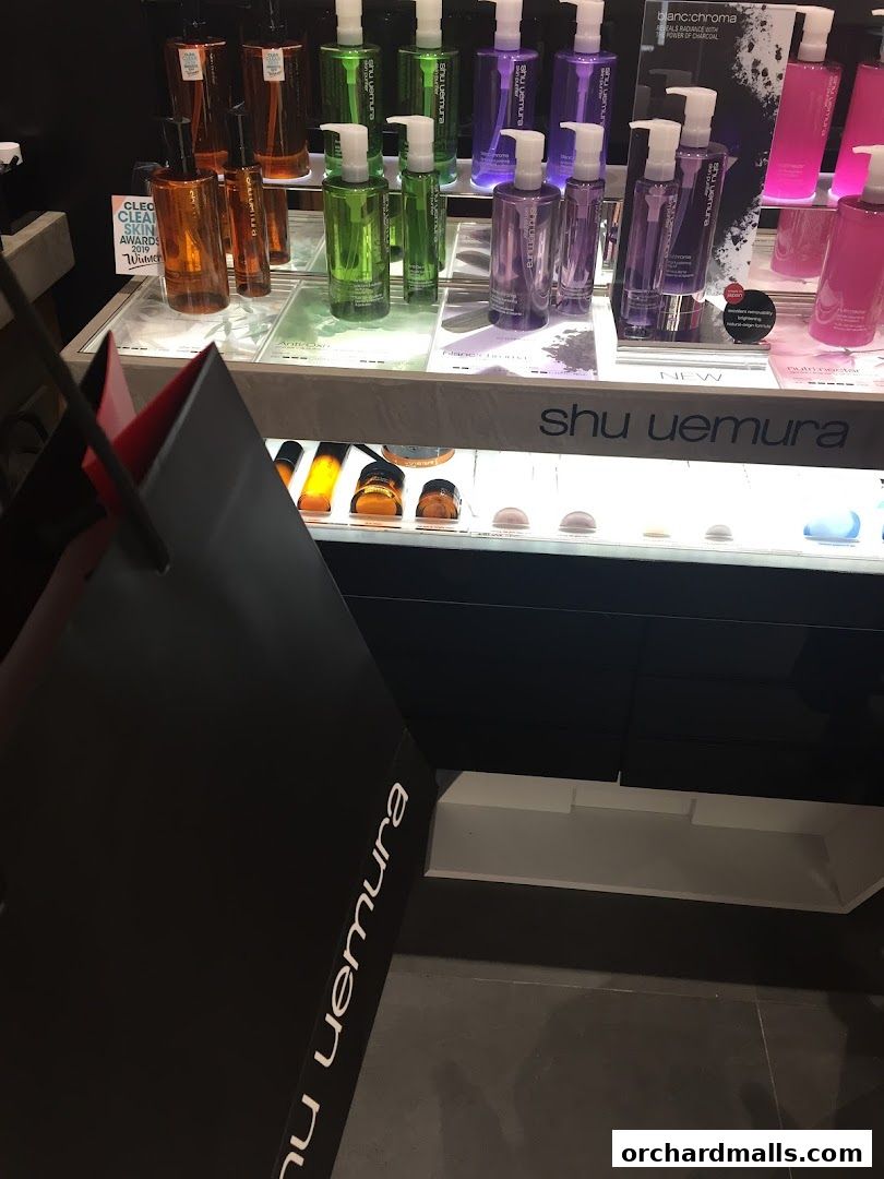 A display of Shu Uemura skincare products, including cleansing oils and serums, with a shopping bag in the foreground.
