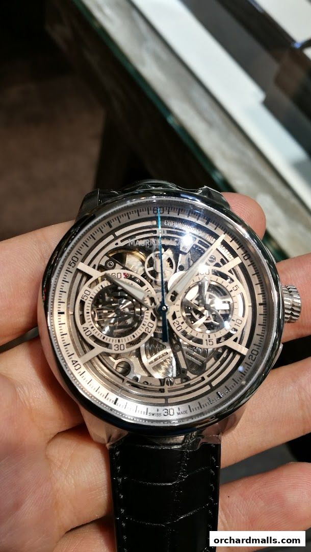 A person holds a detailed, skeletonized luxury watch with a black leather strap.