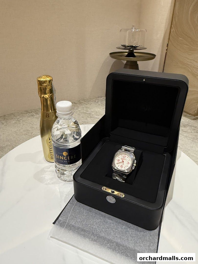 A luxury watch displayed in its box with a bottle of water and a champagne bottle.