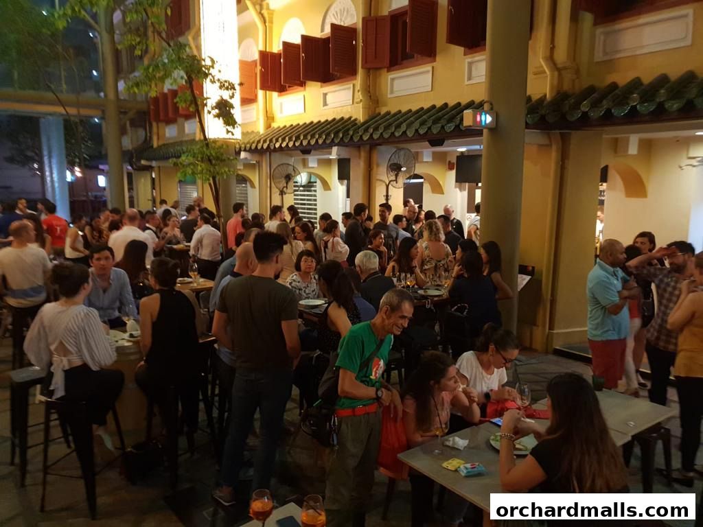 A lively outdoor dining area with many people enjoying drinks and food at tables.