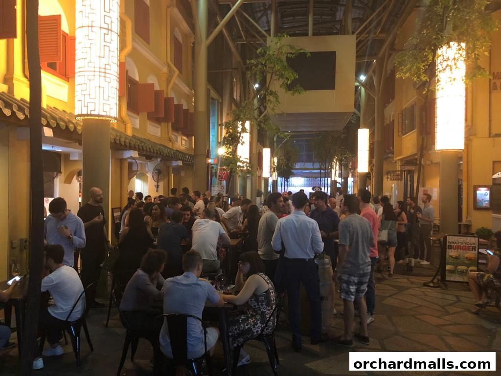 A lively outdoor dining area with many people enjoying food and drinks at tables.