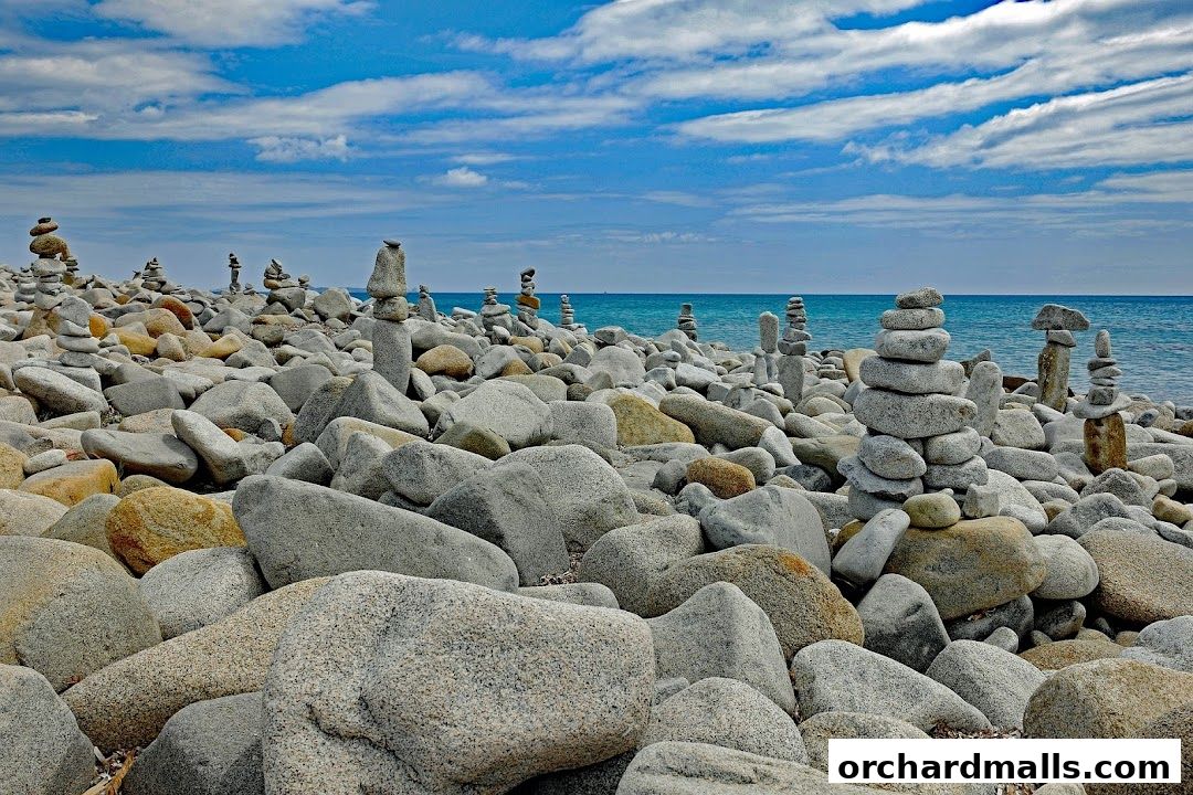 Stone stacks on a rocky beach with the ocean and blue sky in the background.
