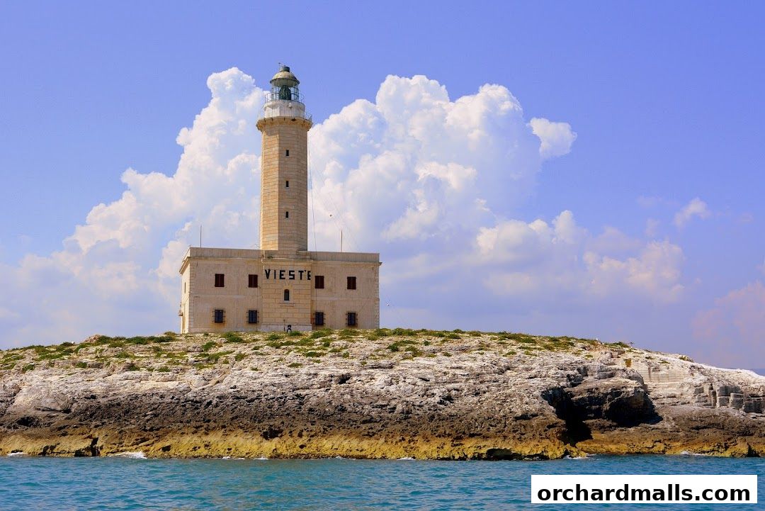 A lighthouse stands tall on a rocky island under a cloudy blue sky.