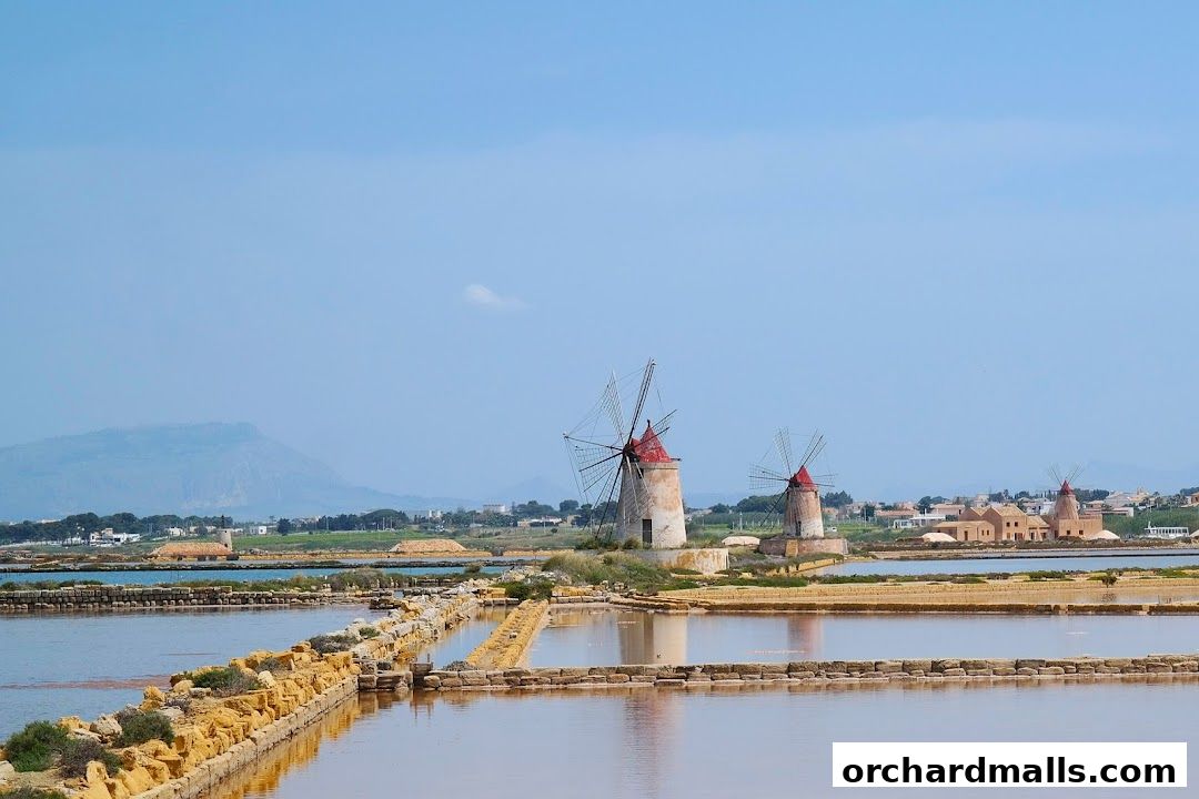 Traditional windmills stand beside salt pans under a clear blue sky.