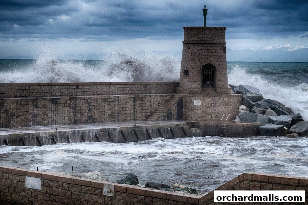 A stone lighthouse stands against a stormy sea with large waves crashing.