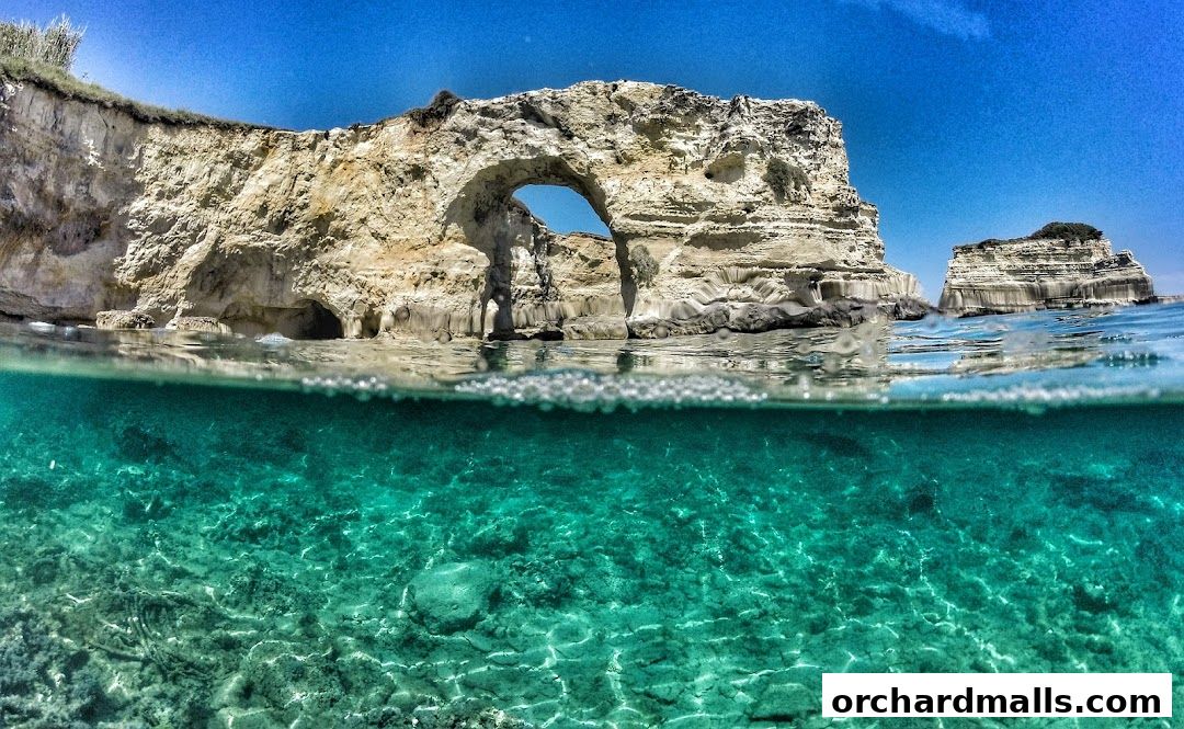 Split view of a rocky coastline with an arch and clear turquoise water.