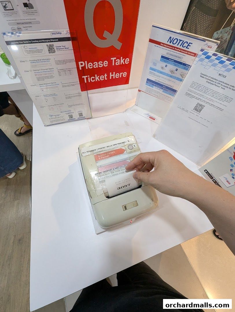 A hand takes a ticket from a queue management machine at Singapore Post.