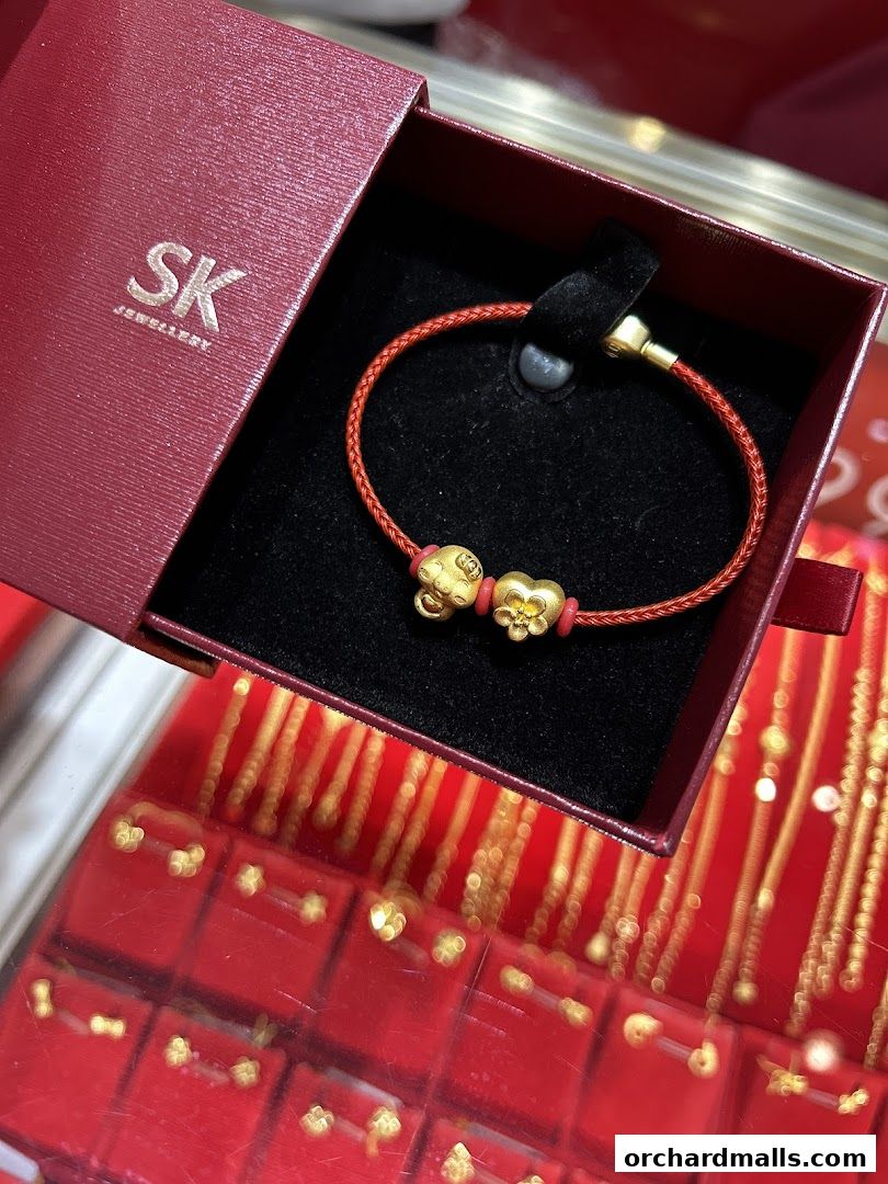 A red jewelry box displays a gold charm bracelet with a red cord and gold charms.