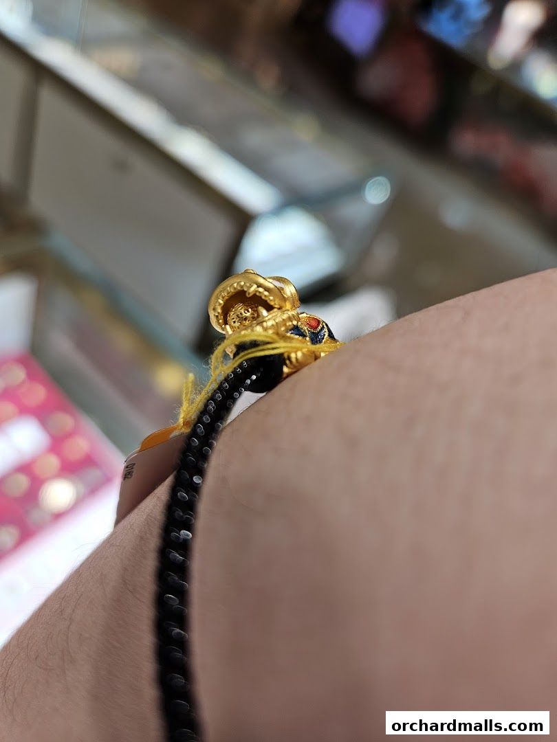 A close-up of a gold pendant on a black beaded bracelet worn on a wrist.