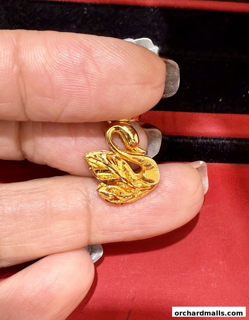 A close-up shot of a delicate gold swan pendant held by fingers.