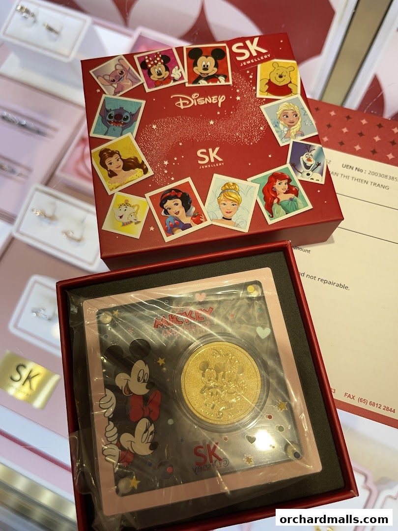 SK Jewellery displays Disney-themed jewelry, including a gold coin featuring Mickey and friends.