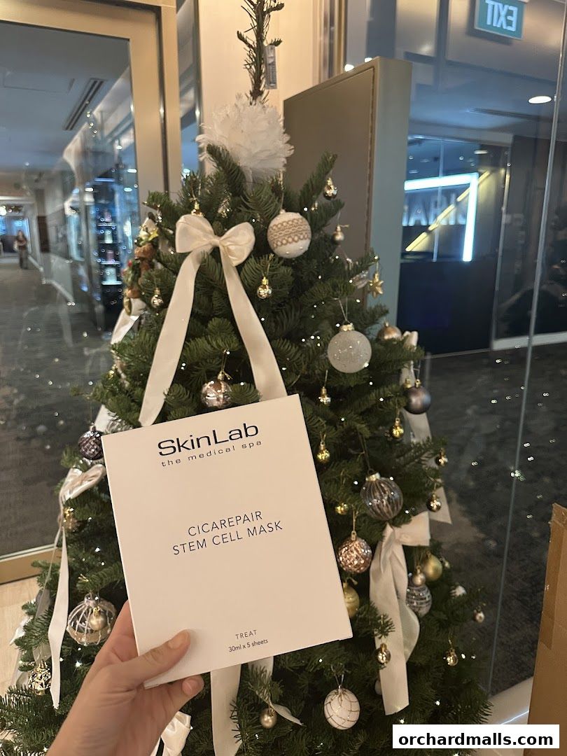 A hand holds a SkinLab Stem Cell Mask in front of a decorated Christmas tree.