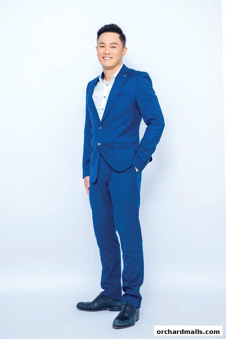 A man in a blue suit and white shirt smiles with his hand in his pocket.