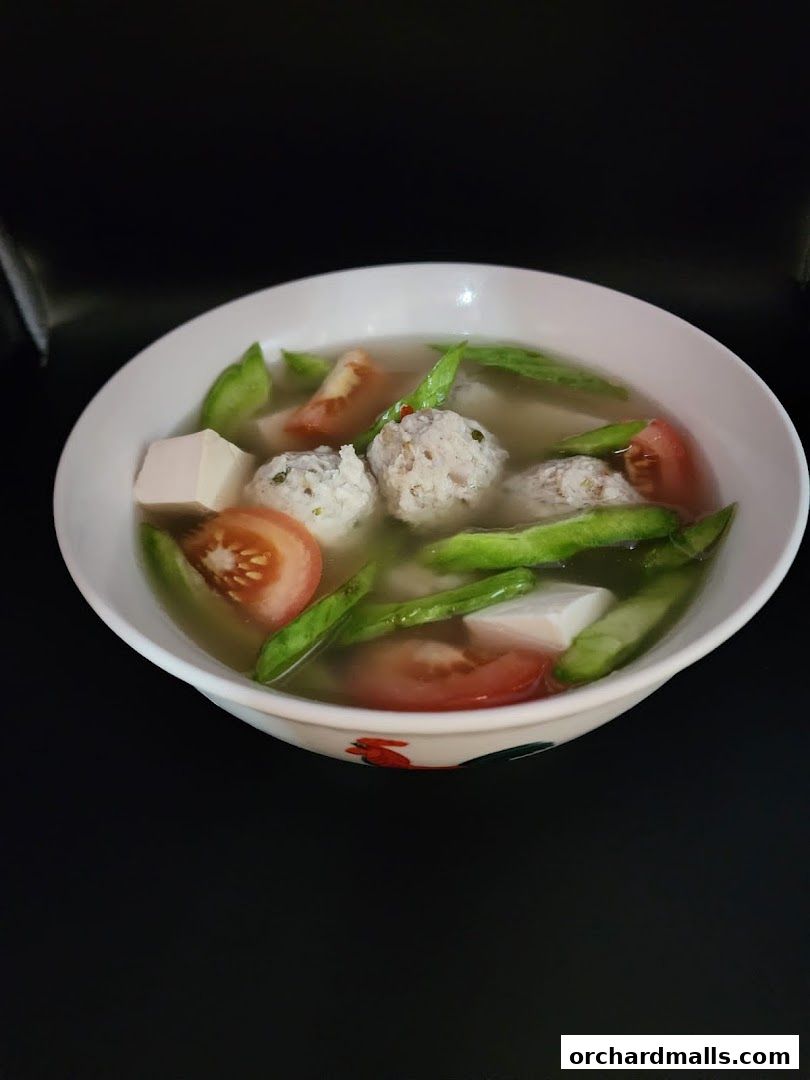 A bowl of fish soup with meatballs, tofu, tomatoes, and green beans.