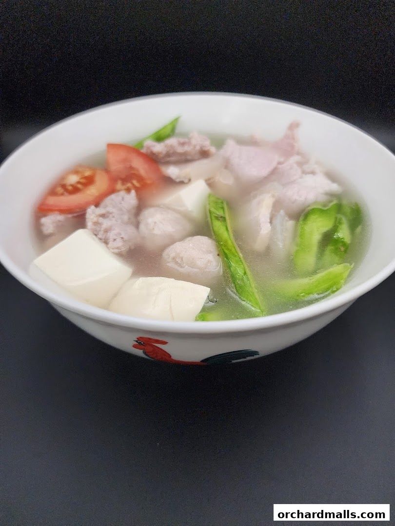 A bowl of fish soup with tofu, tomatoes, meatballs, and vegetables.