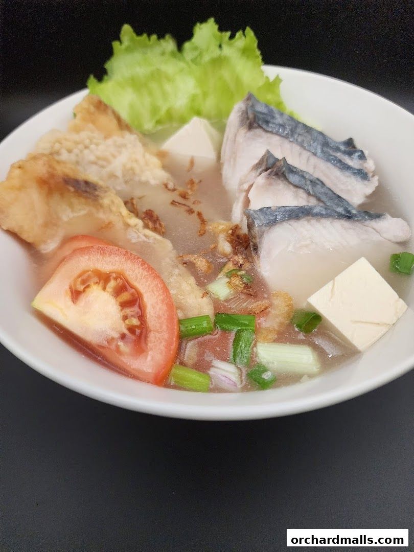 A bowl of fish soup with fish slices, tofu, tomato, and greens.