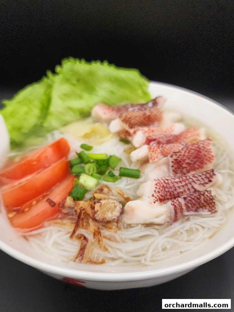 A bowl of fish soup with noodles, tomatoes, lettuce, and fish slices.