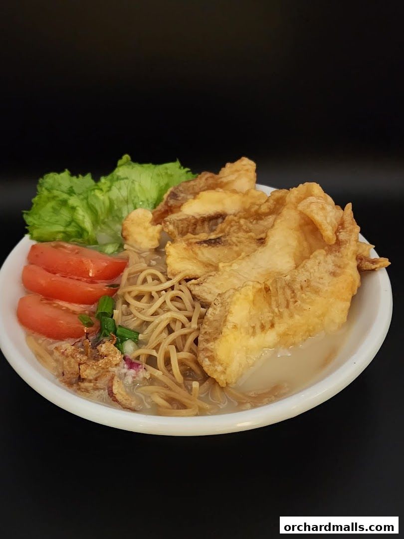 A bowl of fish soup with noodles, fried fish, tomatoes, and lettuce.