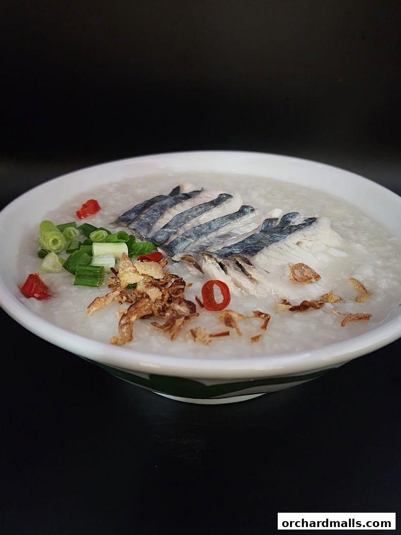 A bowl of fish porridge topped with fish slices, spring onions, and fried shallots.
