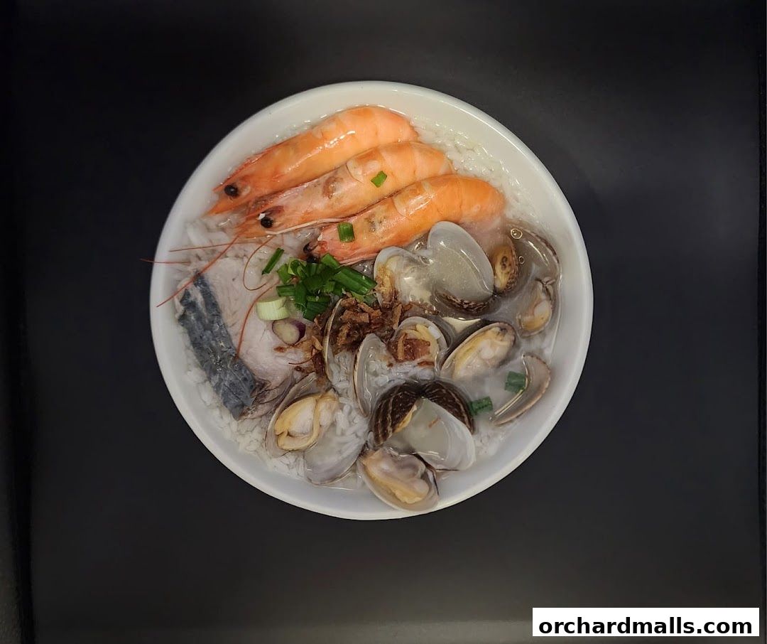 A bowl of seafood congee with prawns, fish, and clams, garnished with spring onions.