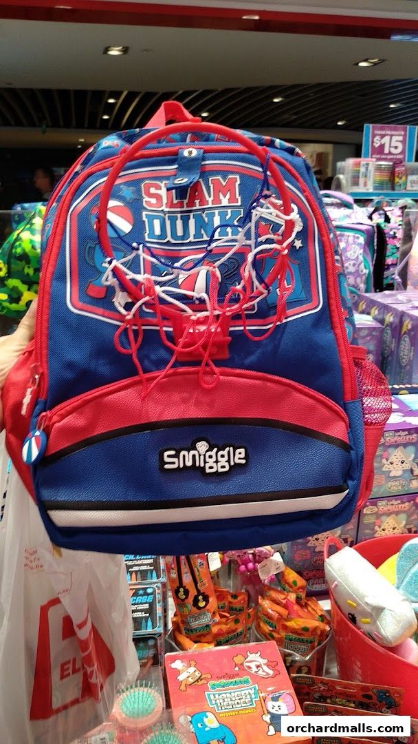 A Smiggle backpack with a 'Slam Dunk' basketball theme, surrounded by other colorful Smiggle products.