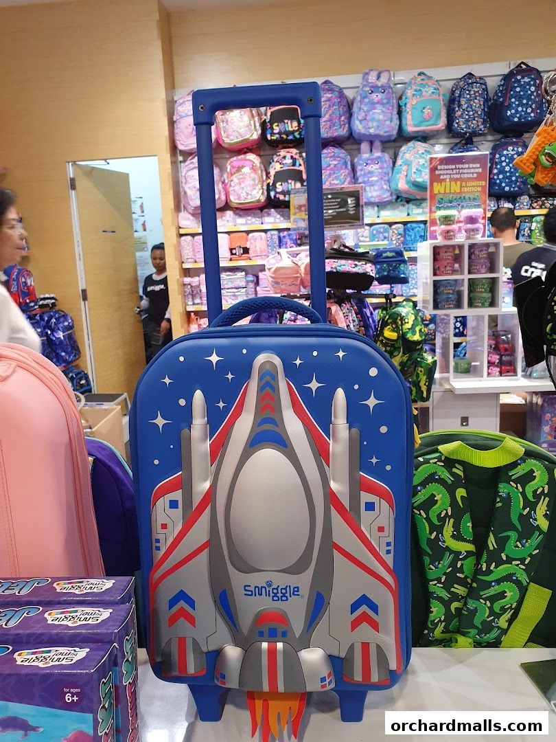 A Smiggle store interior showcasing a blue rolling suitcase with a rocket design and various backpacks.