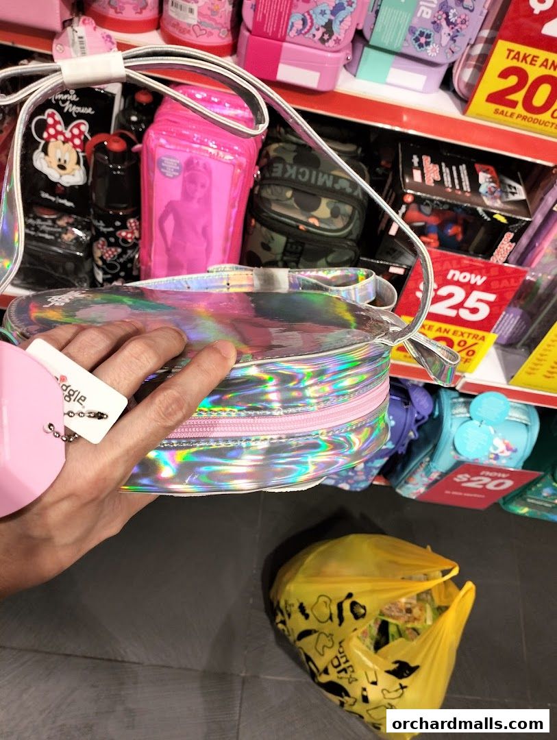 A hand holds a holographic bag in front of shelves stocked with colorful bags and accessories.