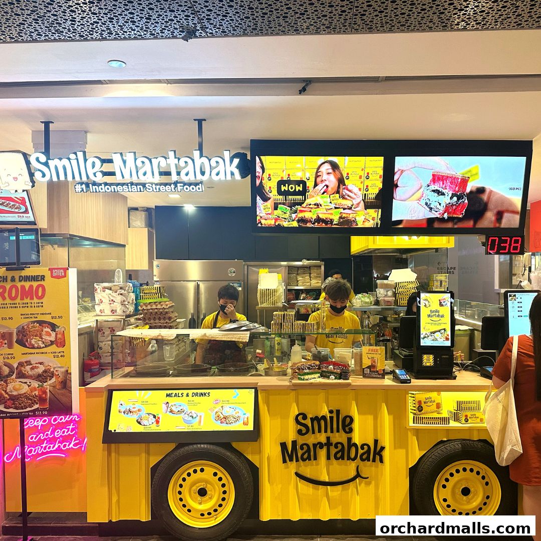 A brightly lit food stall with staff preparing martabak, featuring vibrant displays and signage.