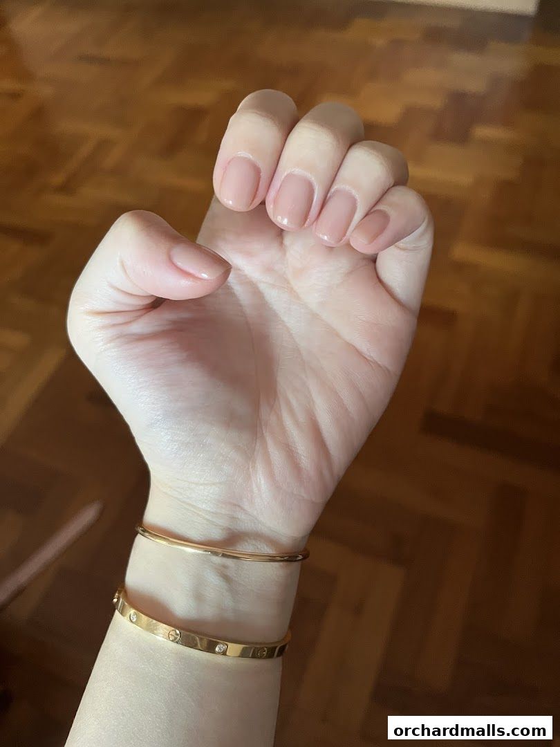 A close-up of a hand with a nude manicure and gold bracelets.