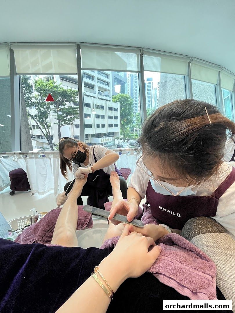 Two technicians are giving pedicures to customers in a bright, modern salon.