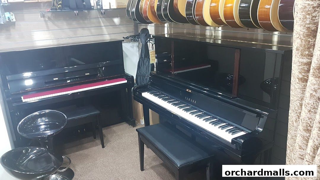 Two upright pianos and a selection of guitars are displayed in a music shop.