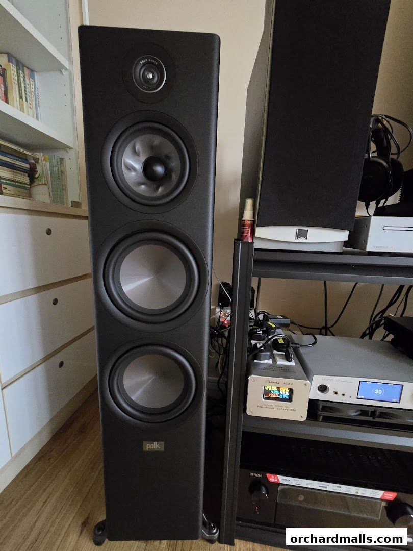A tall black speaker stands next to audio equipment and headphones.