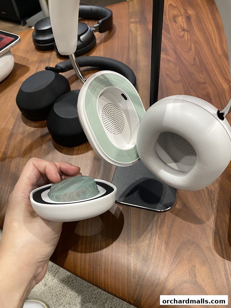 A hand holds a white headphone earcup with a green mesh detail.
