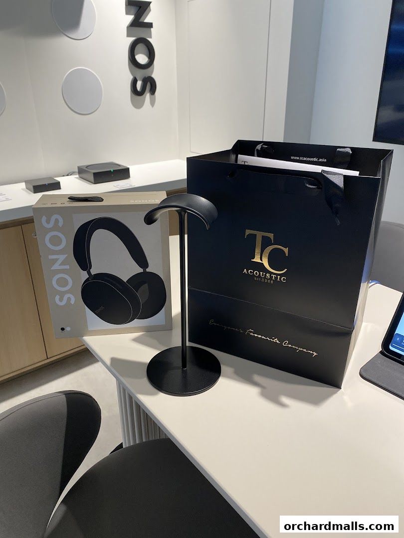 Sonos headphones box, black shopping bag, and display stand on a table.