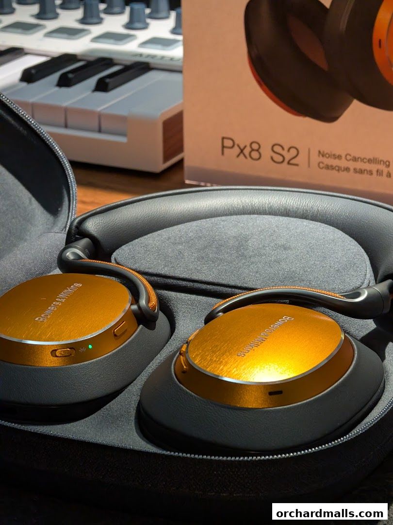 Close-up of premium orange Bowers & Wilkins headphones in a case, with a keyboard and product box.