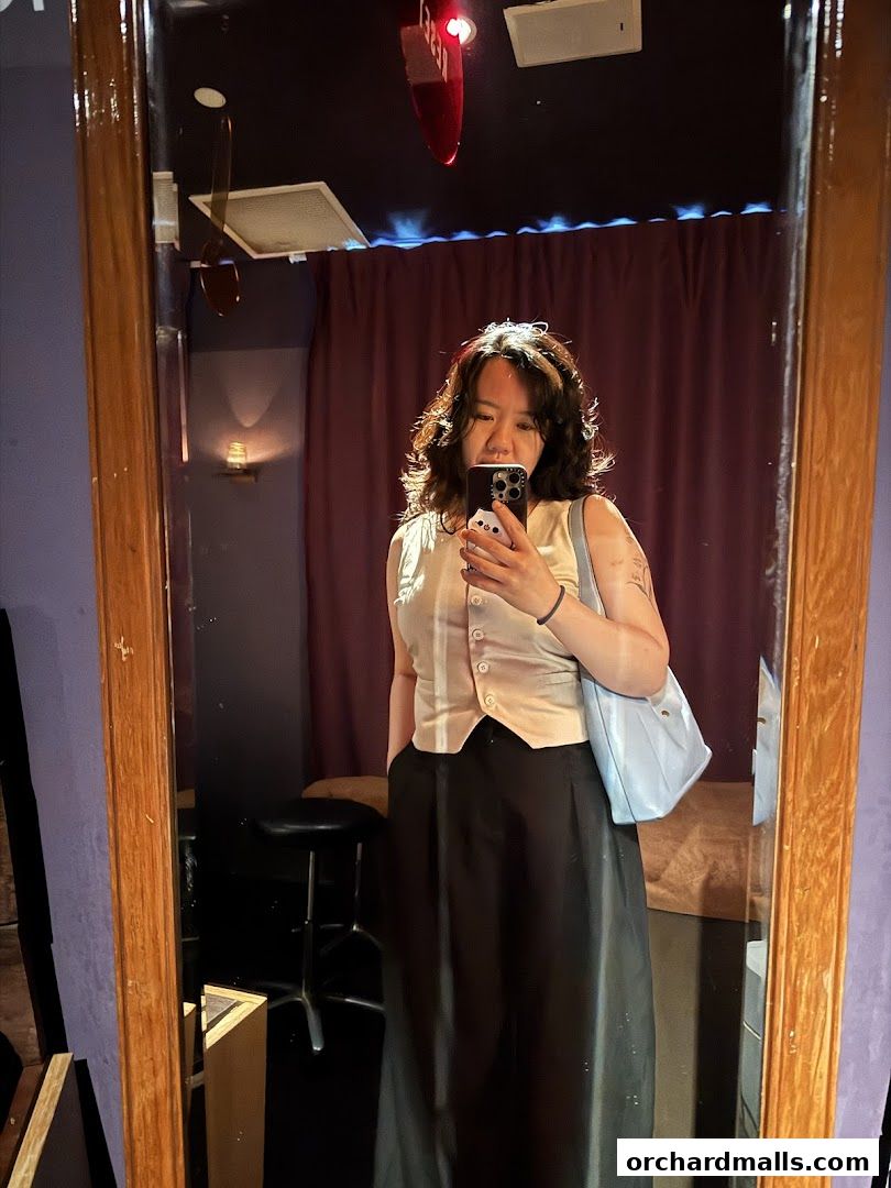A person takes a mirror selfie in a room with purple walls and a red light fixture.